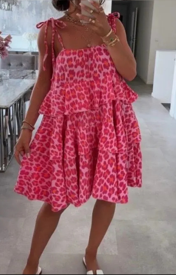 Sommarklänning i rosa och cerise leoprint med knytbara axelband, fotad i dagsljus. Luftig modell i krinklad bomull, one size XS–L.