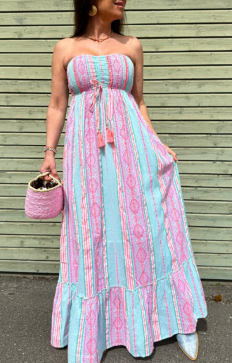 Lång axelbandslös klänning i rosa och turkos med tofsar framtill under bysten. Tillverkad i 100% bomull. One size passar XS till M.