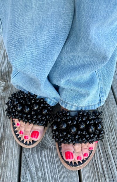 Svarta slipperssandaler med dekorativa svarta pärlor och zigzagbroderier – en elegant sko som passar både till fest och vardag.