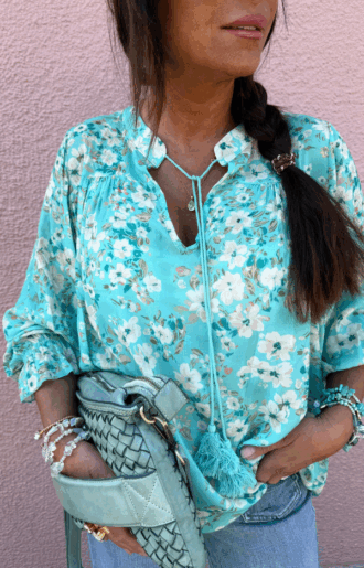 Susanne Blouse i aqua-turkos med offwhite blommor, viskosblus med långa bomullstassels vid halsen, volang och resår vid ärmarna.