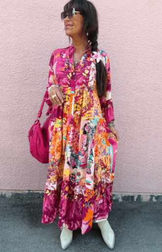 Solene viskosklänning i cerise med abstrakt print, lång modell i viskos med kort ärm och vackert fall, fotad framifrån på modell i sommarmiljö.