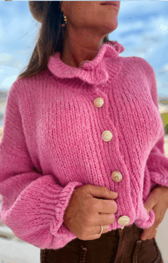 Stickad kofta i cerise med guldknappar och volanger vid hals och ärmslut. Mjuk, färgstark design i one size som passar XS–L.