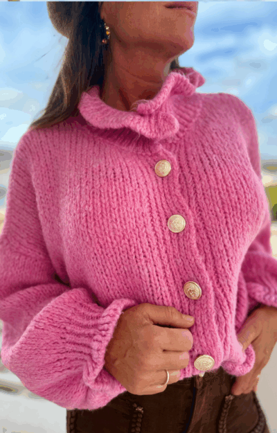 Stickad kofta i cerise med guldknappar och volanger vid hals och ärmslut. Mjuk, färgstark design i one size som passar XS–L.