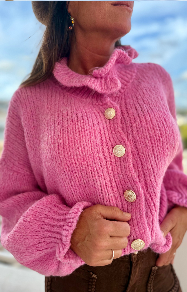 Stickad kofta i cerise med guldknappar och volanger vid hals och ärmslut. Mjuk, färgstark design i one size som passar XS–L.
