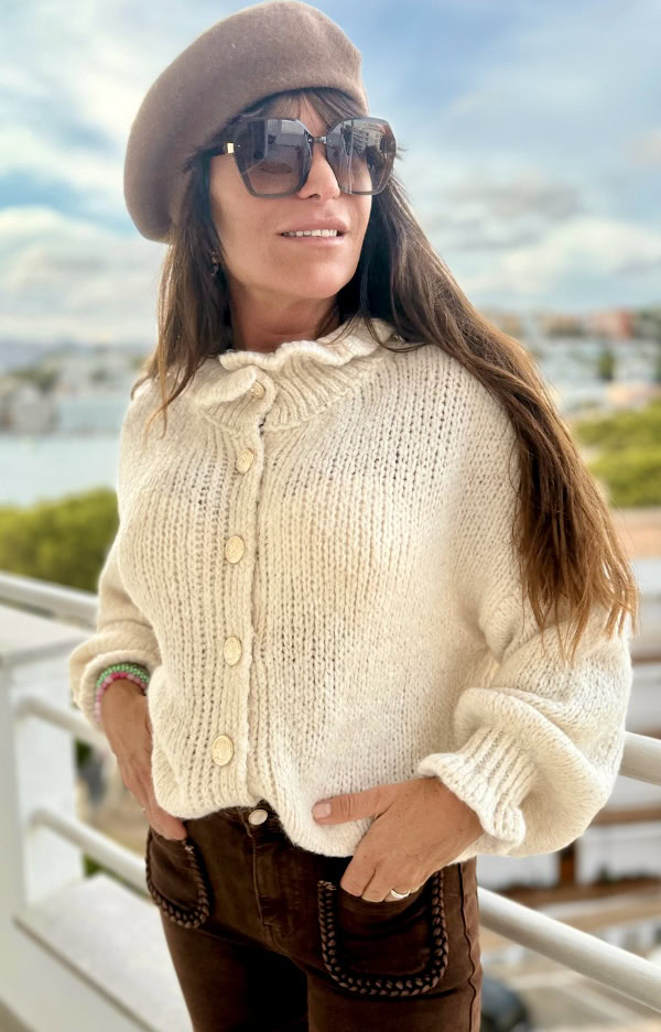 Stickad kofta i krämigt beige med volanger vid hals och ärmslut samt guldknappar framtill. Lyxig och mjuk design i one size, passar XS–L.
