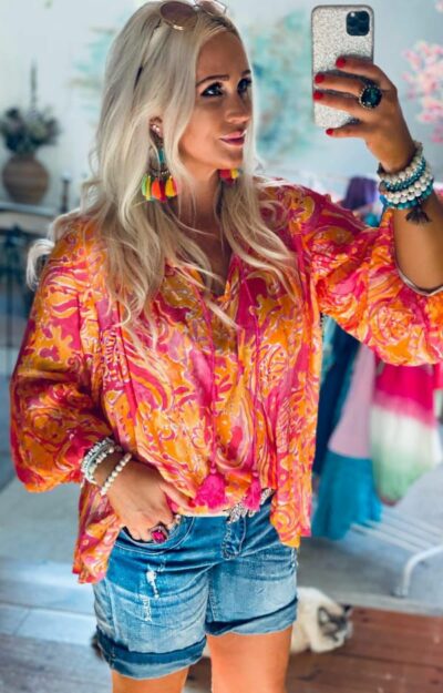 Susanne Blouse i färgstarkt cerise och orange print, viskosblus med långa bomullstassels vid halsringningen och volangärmar.