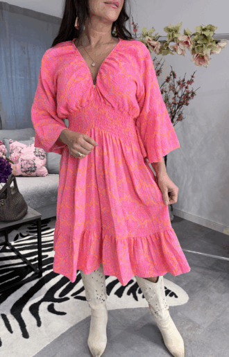 Klänning med neonrosa print i 100% bomull, krinklad, med smickrande smock under byst och resår vid halsringning på modell.
