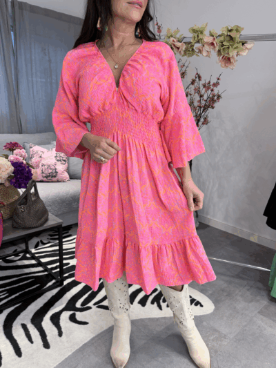 Klänning med neonrosa print i 100% bomull, krinklad, med smickrande smock under byst och resår vid halsringning på modell.