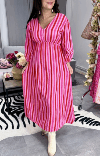 Randig klänning i rosa och rött i 100% bomull på modell, smickrande passform med resår och justerbart nackband.