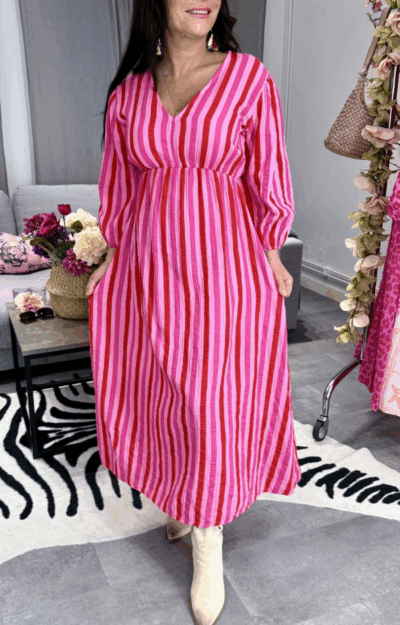 Randig klänning i rosa och rött i 100% bomull på modell, smickrande passform med resår och justerbart nackband.