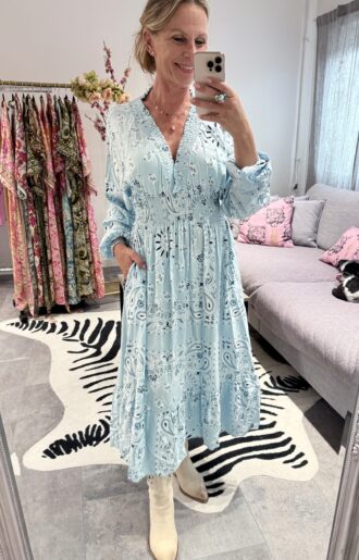 Klänning i viskos med bandanaprint i ljusblå, rosa och coral, med volang och fickor.