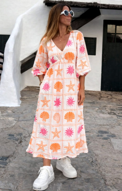 Sommarklänning med vit botten och rosa & orange print med snäckor och solar på modell, smickrande passform med resår och justerbart nackband.