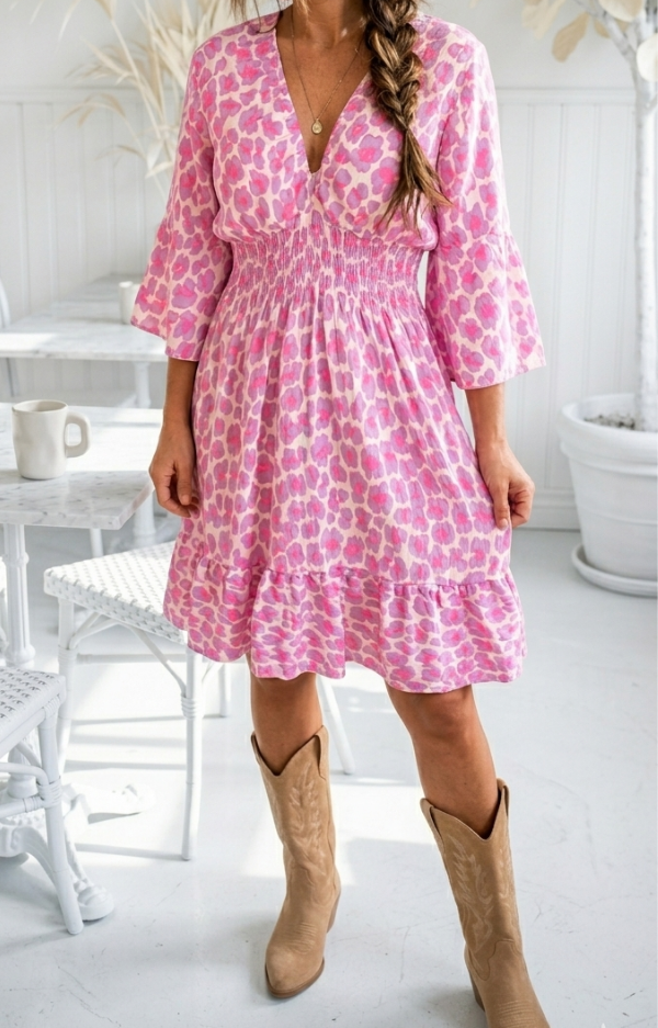 Klänning med neonrosa print i 100% bomull, krinklad, med smickrande smock under byst och resår vid halsringning på modell.